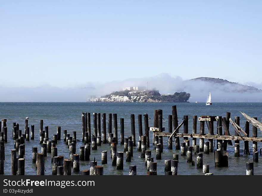 Alcatraz Prison fogged over on a sunny day. Old pilings in foreground. Alcatraz Prison fogged over on a sunny day. Old pilings in foreground.