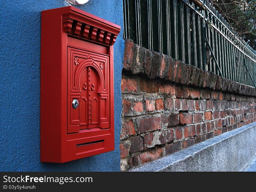 Red metal post box on brick wall and iron fence