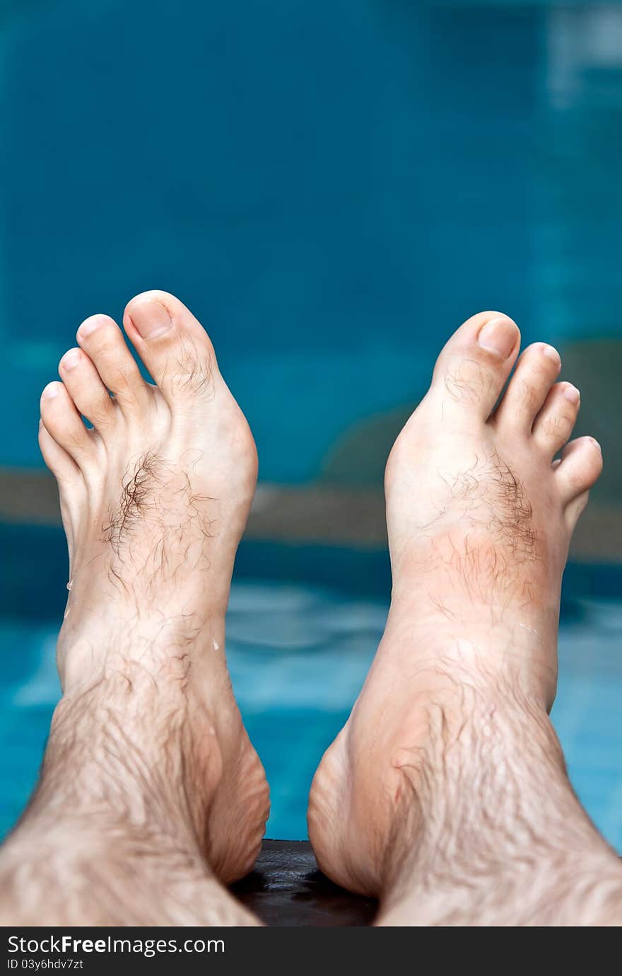 Men's feet on the background of the pool with blue water