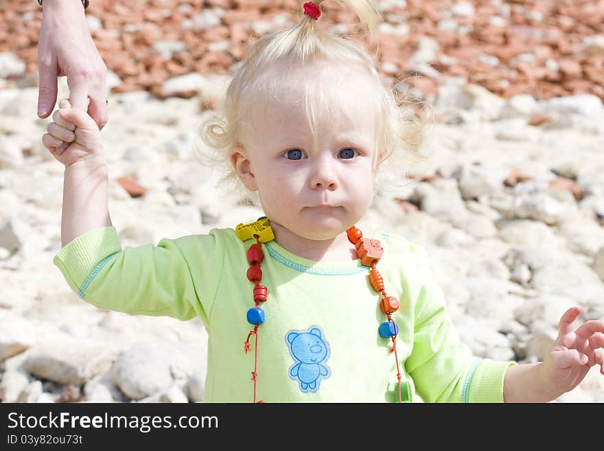 Serious blue-eyed toddler making her first steps while holding on her mother's finger.