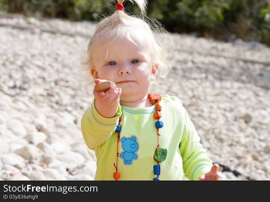 Cute baby girl holding out a pebble to play.