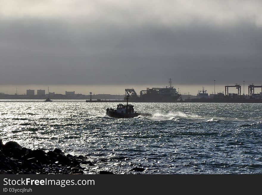 A tug boat leaves Cape Town harbor in choppy waters. A tug boat leaves Cape Town harbor in choppy waters