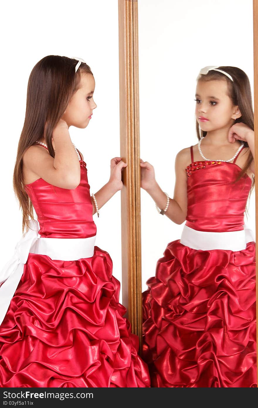 Beautiful little girl in red evening dress in front of mirrow on white background