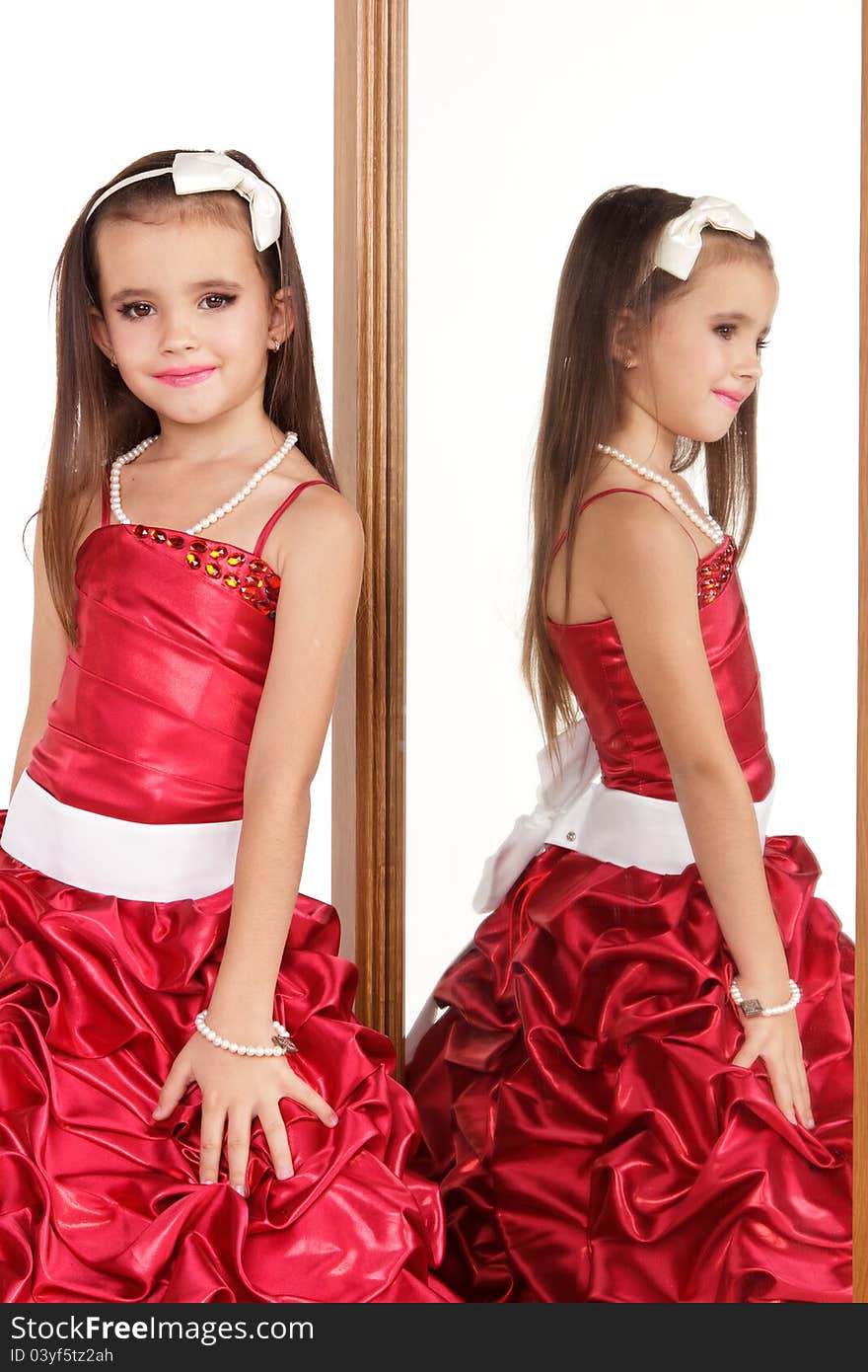 Beautiful little girl in red evening dress in front of mirrow on white background