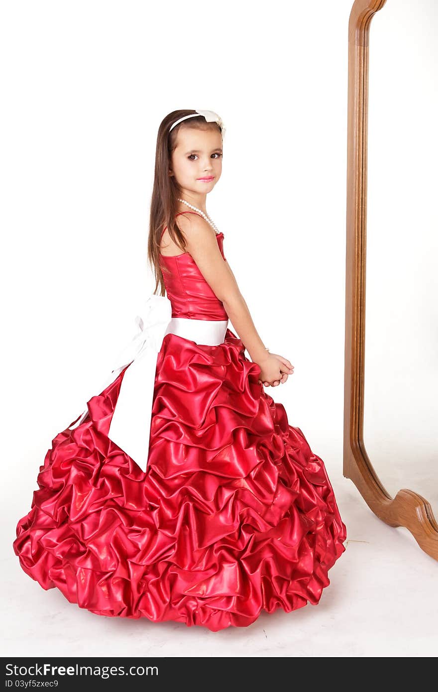 Beautiful little girl in red evening dress in front of mirrow on white background