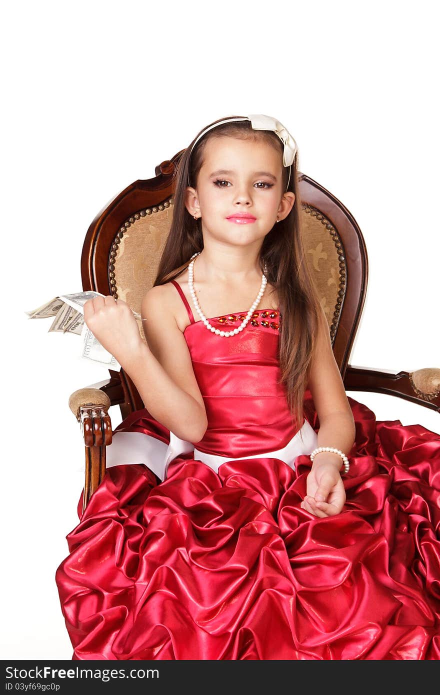 Beautiful little girl in red evening dress sitting on chair with money as fan on white background