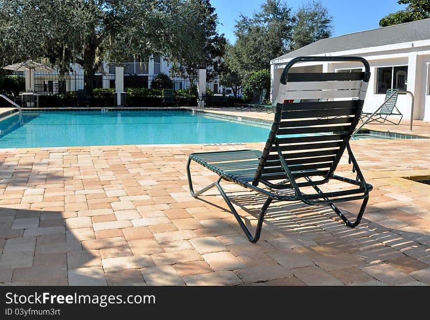 Green pool chair in front of a swimming pool on a sunny summer day.