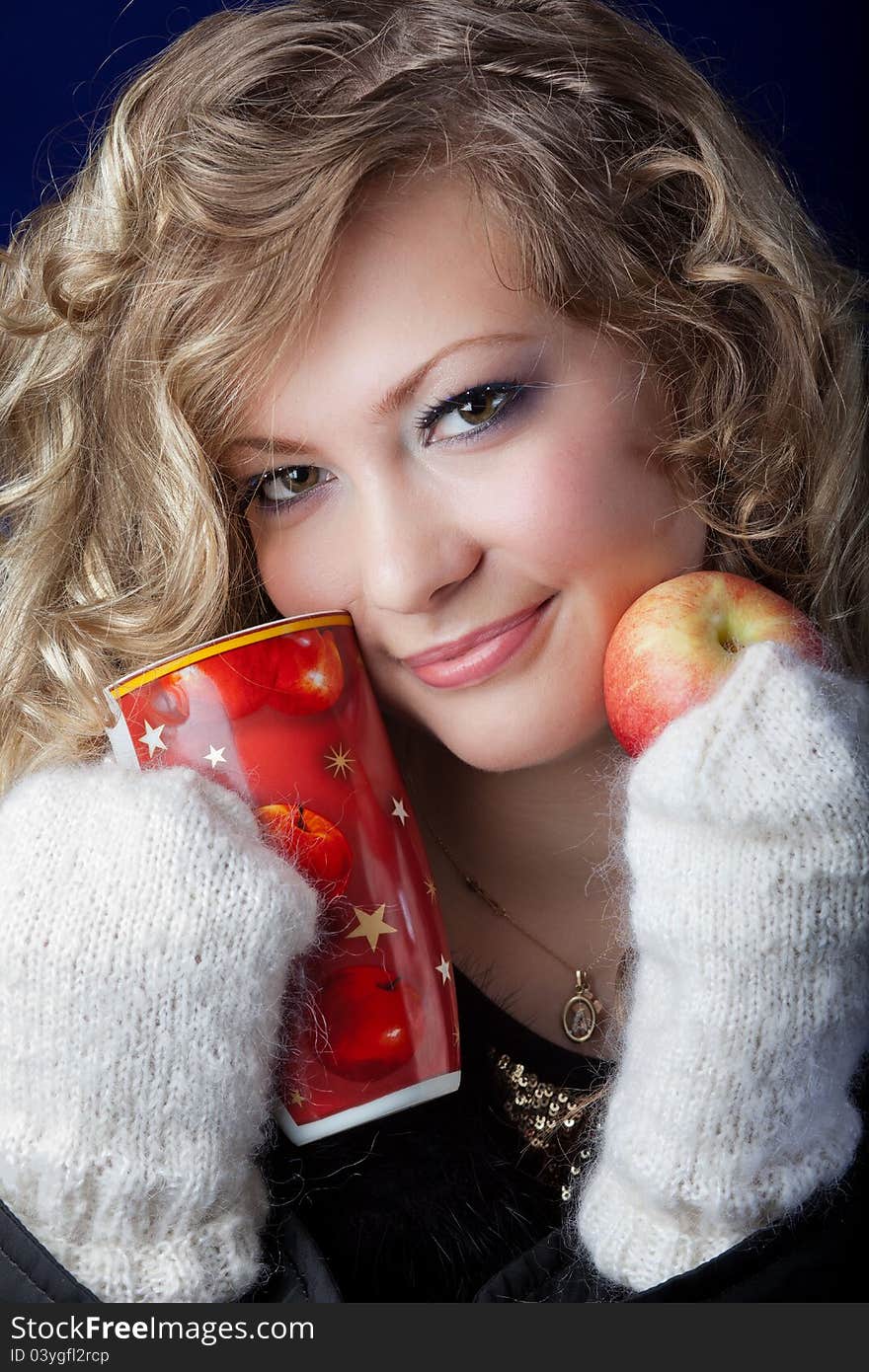 Girl with a long fair hair in knitted mittens and an apple in hands. Girl with a long fair hair in knitted mittens and an apple in hands