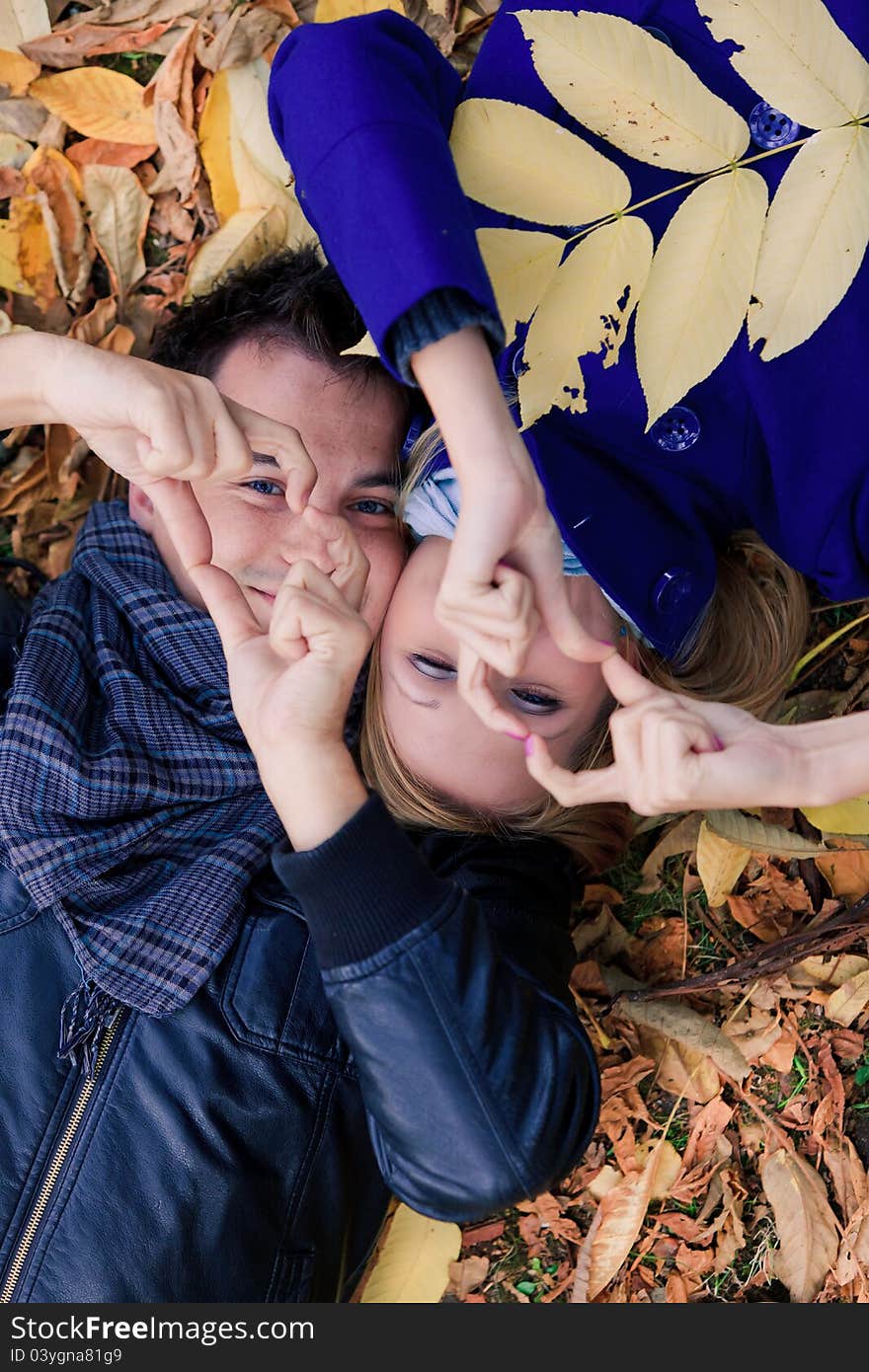 Portrarit of a happy young couple lying on fallen leaves with hands up in the park. Portrarit of a happy young couple lying on fallen leaves with hands up in the park.