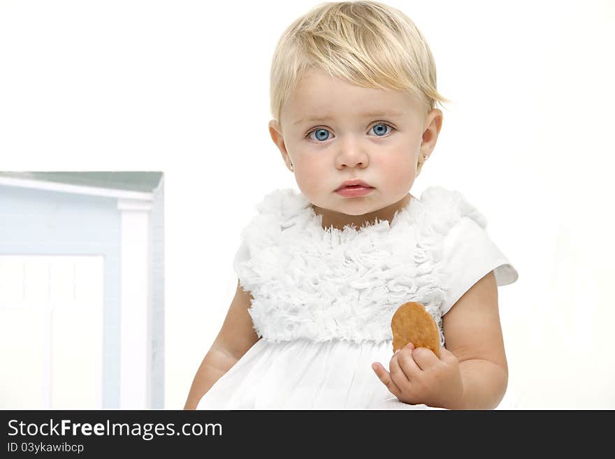 Blue eyed baby girl with boring expression holding a biscuit. Isolated on white background. Blue eyed baby girl with boring expression holding a biscuit. Isolated on white background.