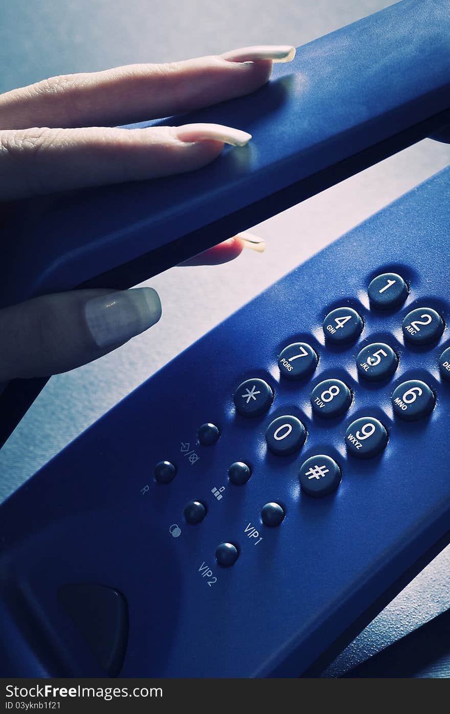 A woman's hand picking up the handset of an  blue phone. A woman's hand picking up the handset of an  blue phone