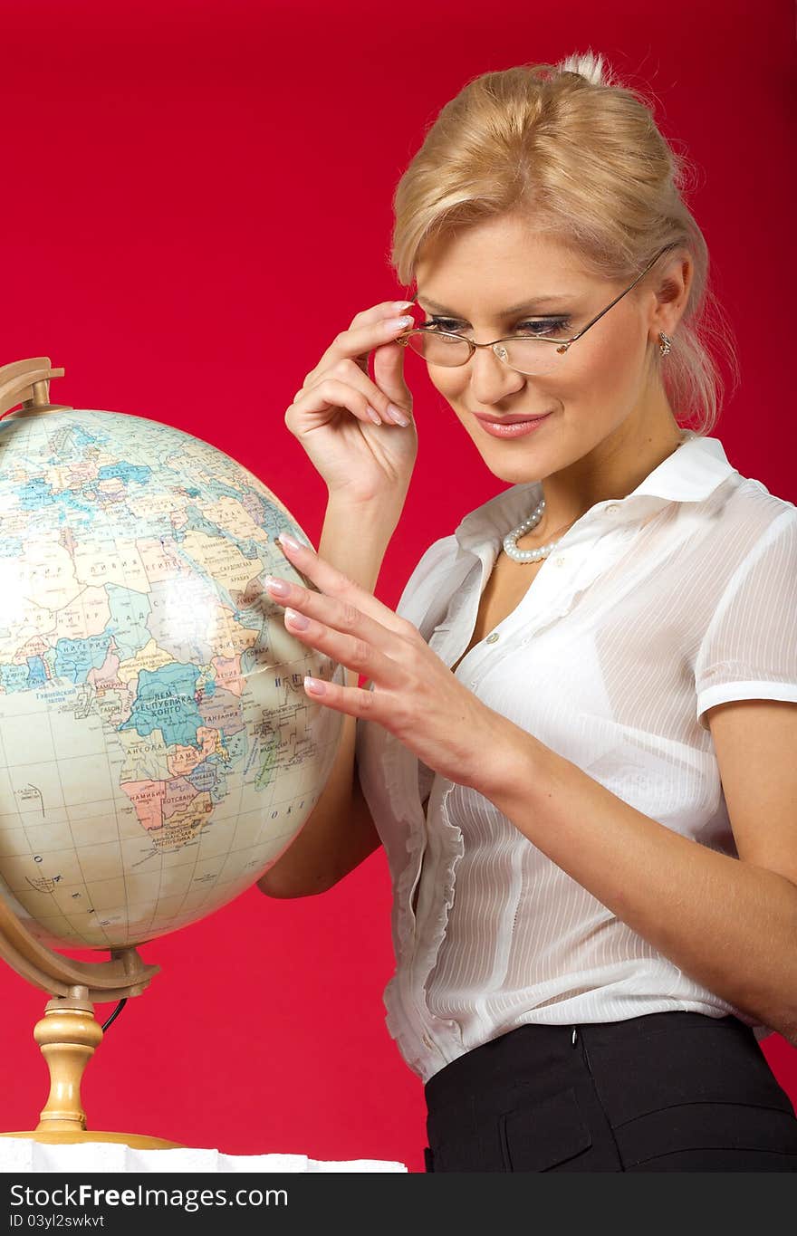 Pretty woman teacher with globe posing in studio on red background