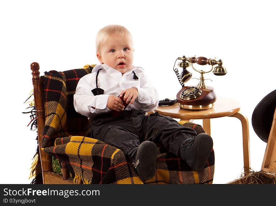 Cute baby boy sitting in a chair with retro telephone