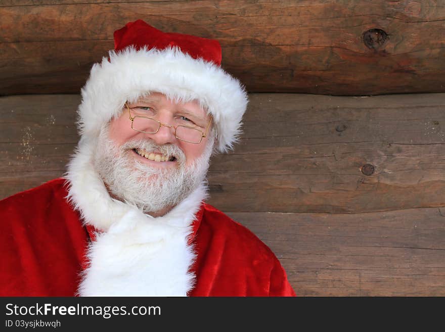 Smiling Santa Claus in front of a log cabin wall. Smiling Santa Claus in front of a log cabin wall.