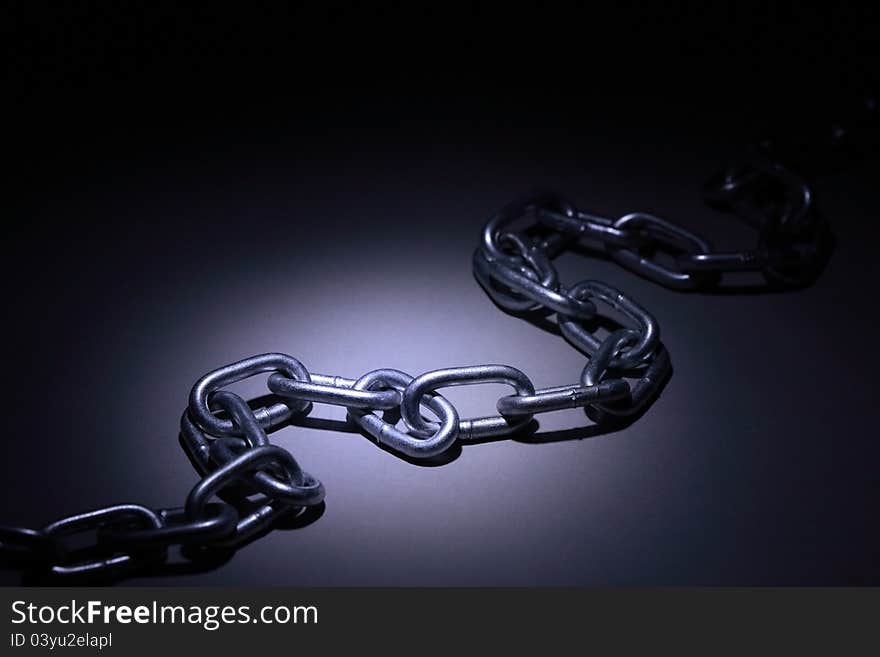 Closeup of metal chain under beam of light on dark background. Closeup of metal chain under beam of light on dark background