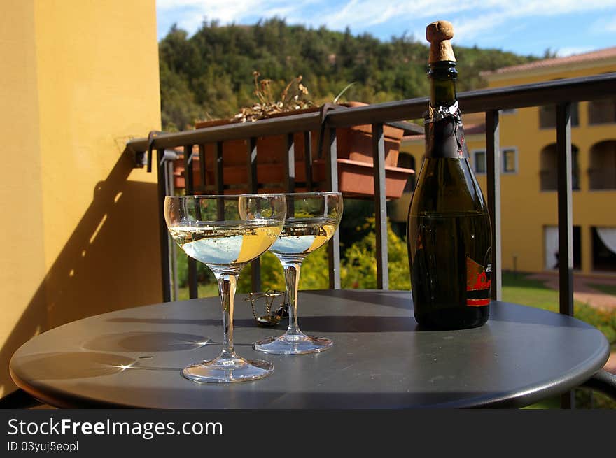 Two full champagne glasses in front of a black of sparkling white wine on a table outdoors on a summer morning at the hotel. Two full champagne glasses in front of a black of sparkling white wine on a table outdoors on a summer morning at the hotel.