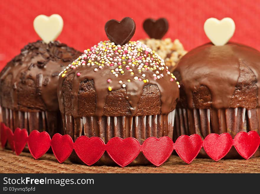 Four Valentine muffins with white and dark chocolate hearts, on wrapped with red fabric hearts