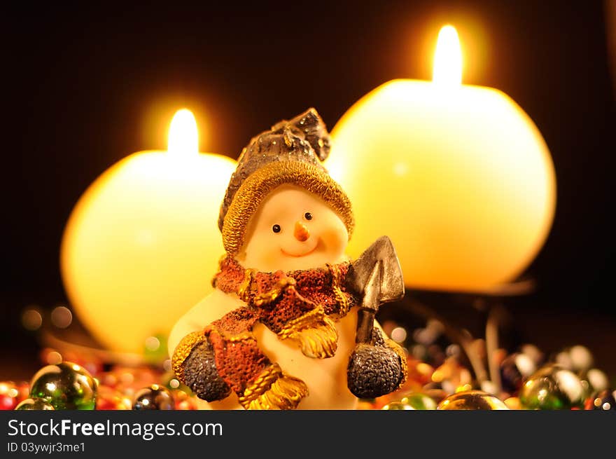 A smiling snowman figurine and burning candles on a black background