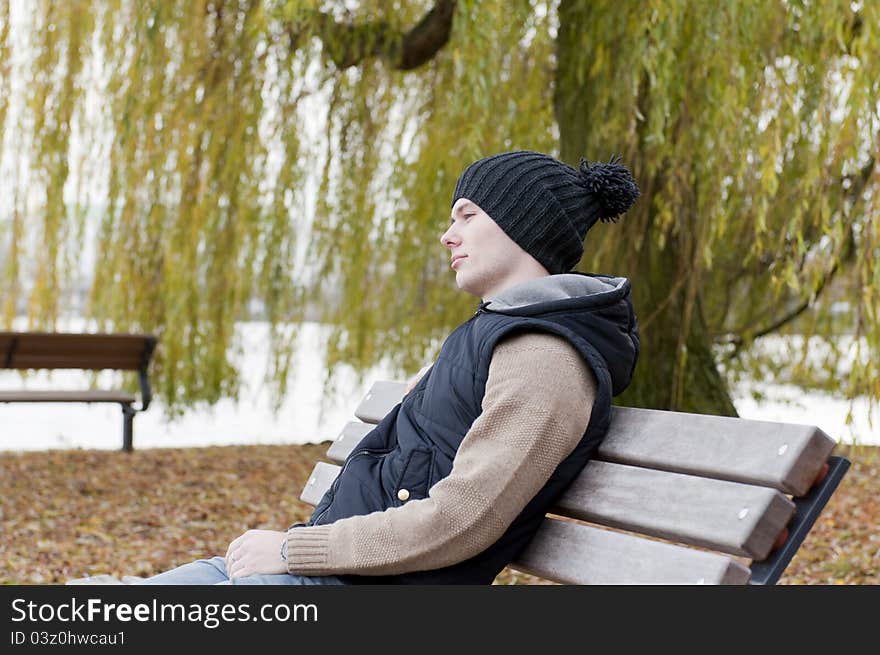 Man sits on the bench in the park on the background of leaves and willow tree