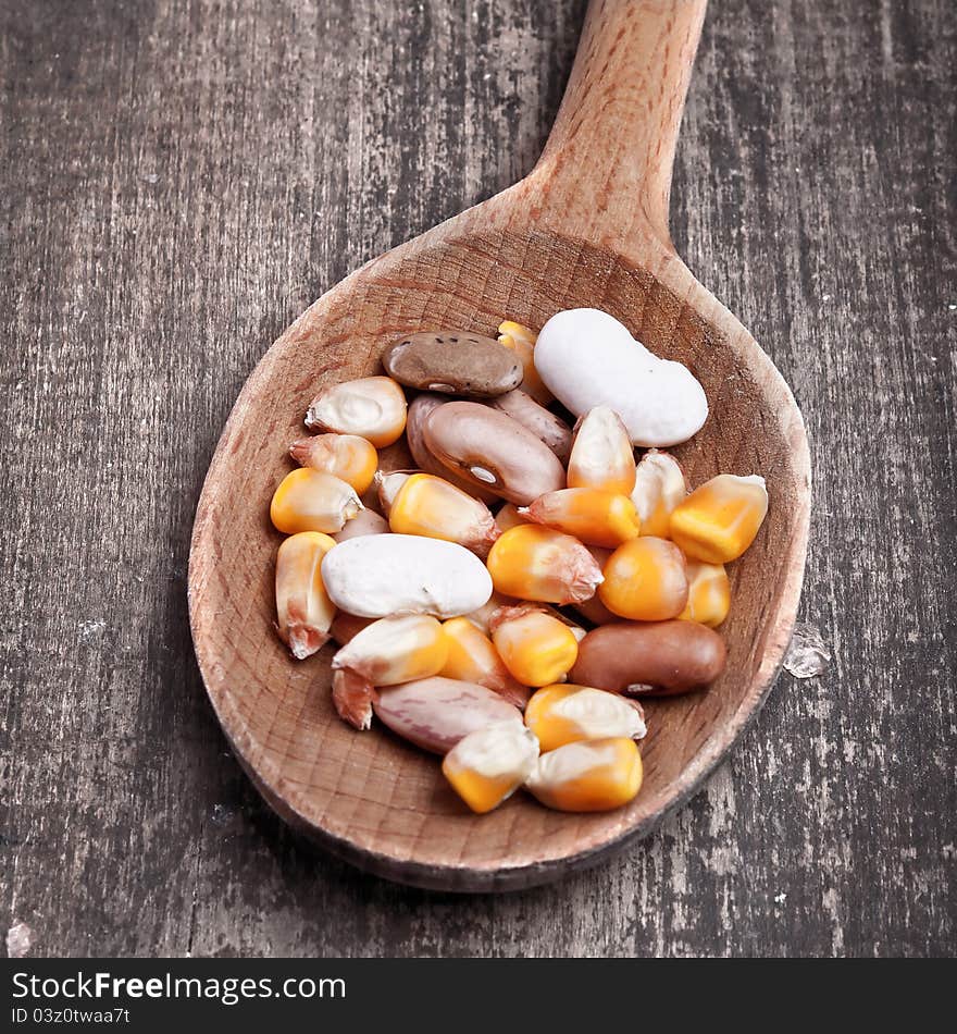 Wooden spoon with beans and corn on wooden plank