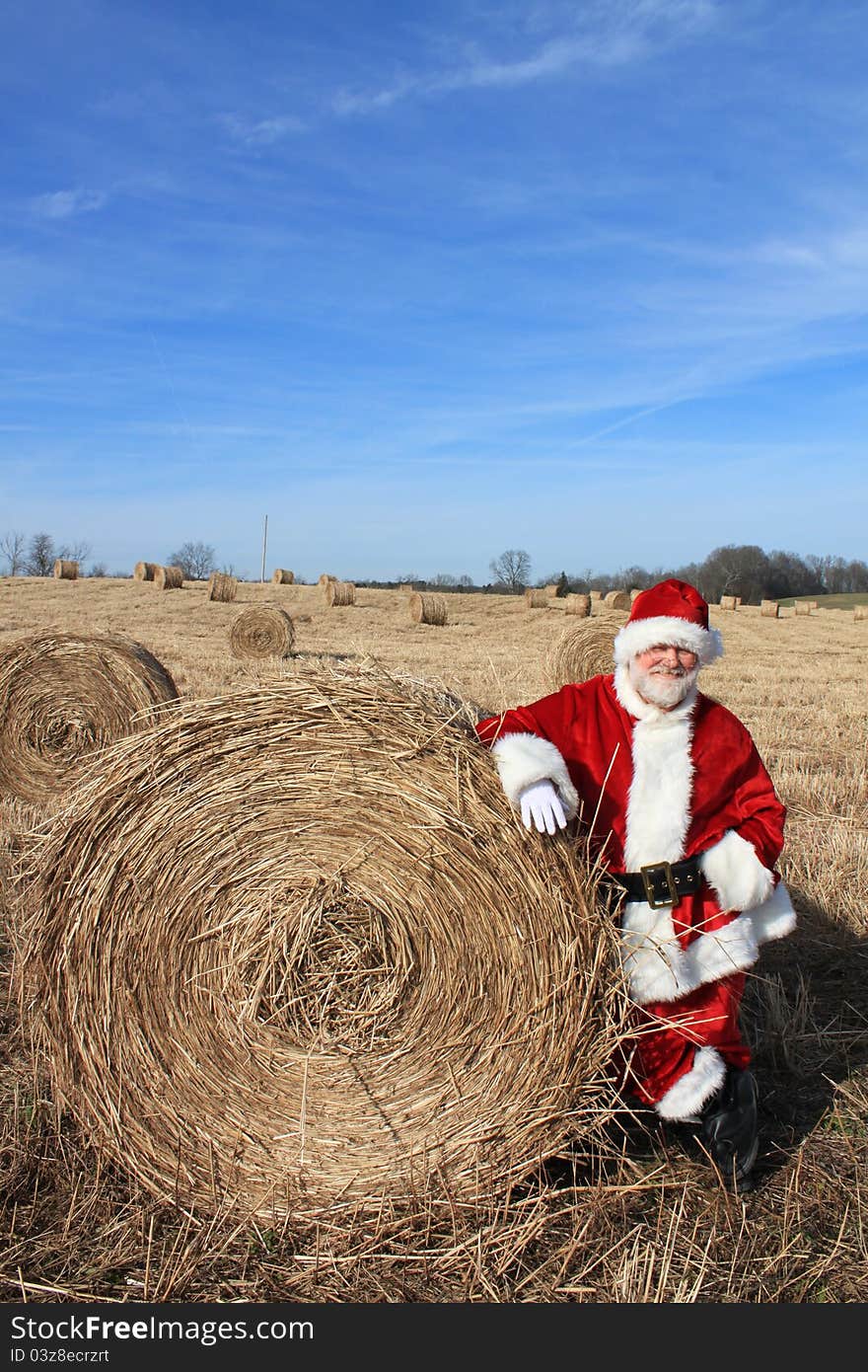 Santa Claus standing against a bale of hay in a hay field. Santa Claus standing against a bale of hay in a hay field.