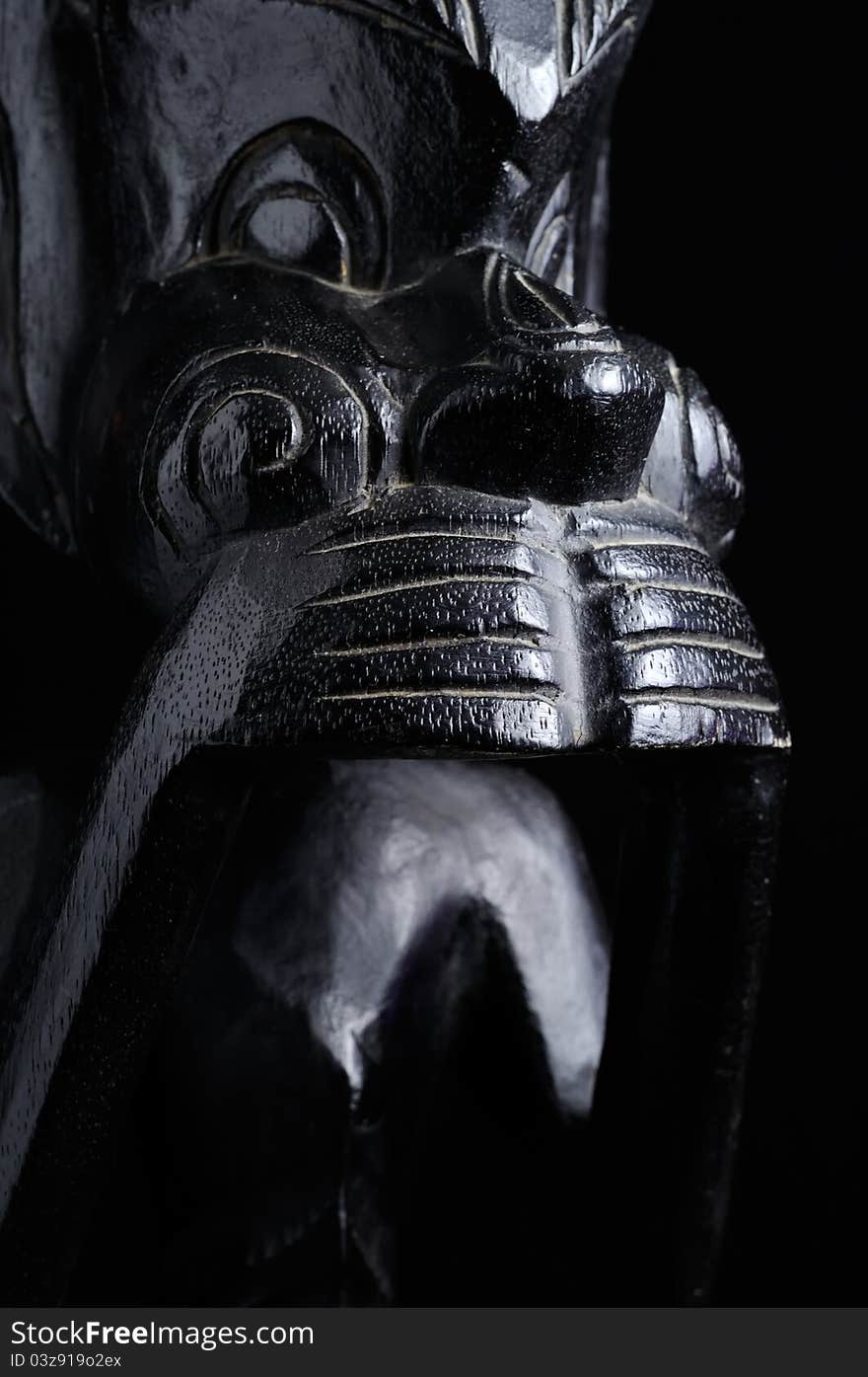 A black wooden statuette covering its mouth with hands symbolizing silence