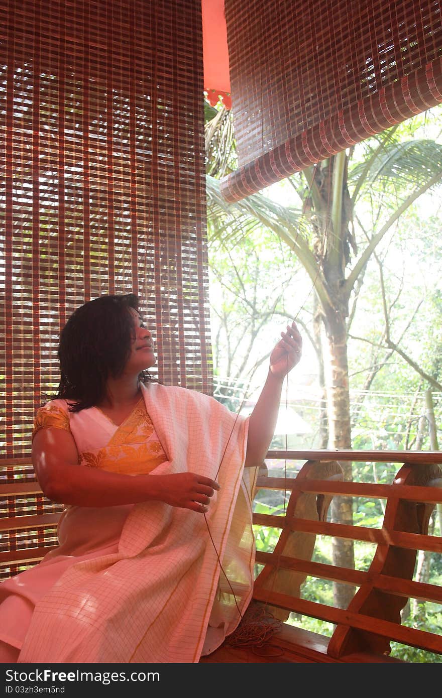 Beautiful Indian Girl Raising Bamboo Curtain from her balcony to have a clear look outside.