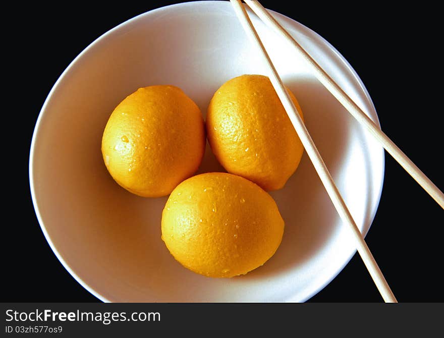 Three lemons in a bowl with chopsticks