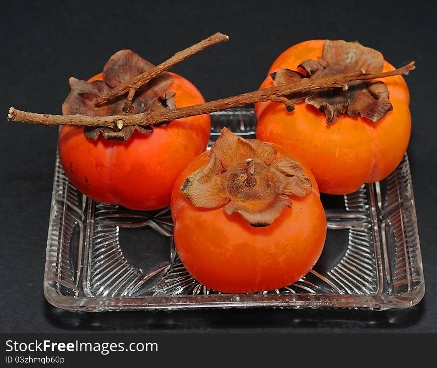 Persimmons in glass dish on a black background