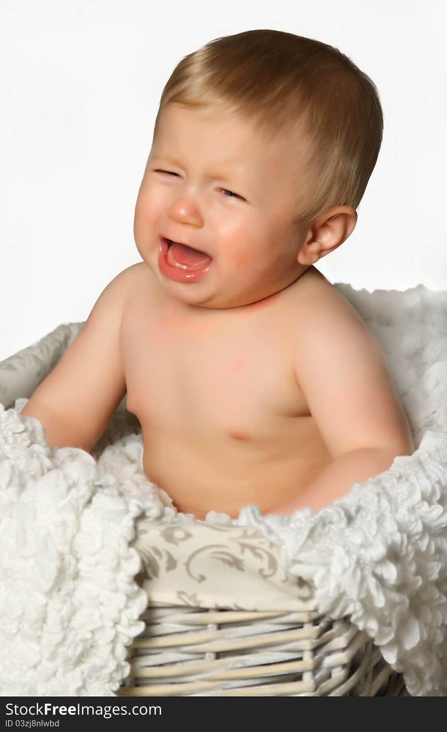 A little boy sitting in a straw basket with a blanket and crying. A little boy sitting in a straw basket with a blanket and crying.