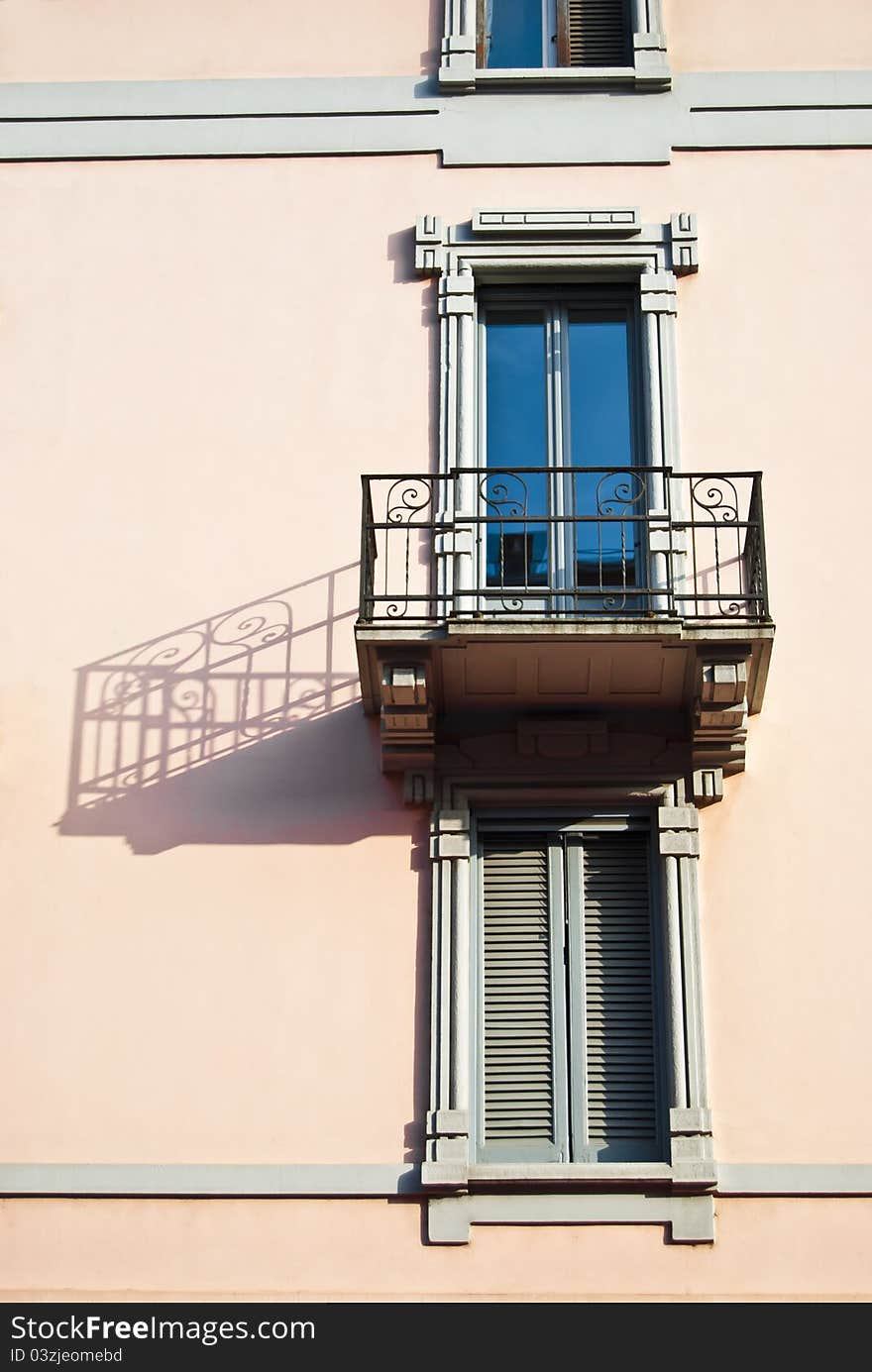 Old elegant balcony of a pink palace with lateral long and dramatic shadow