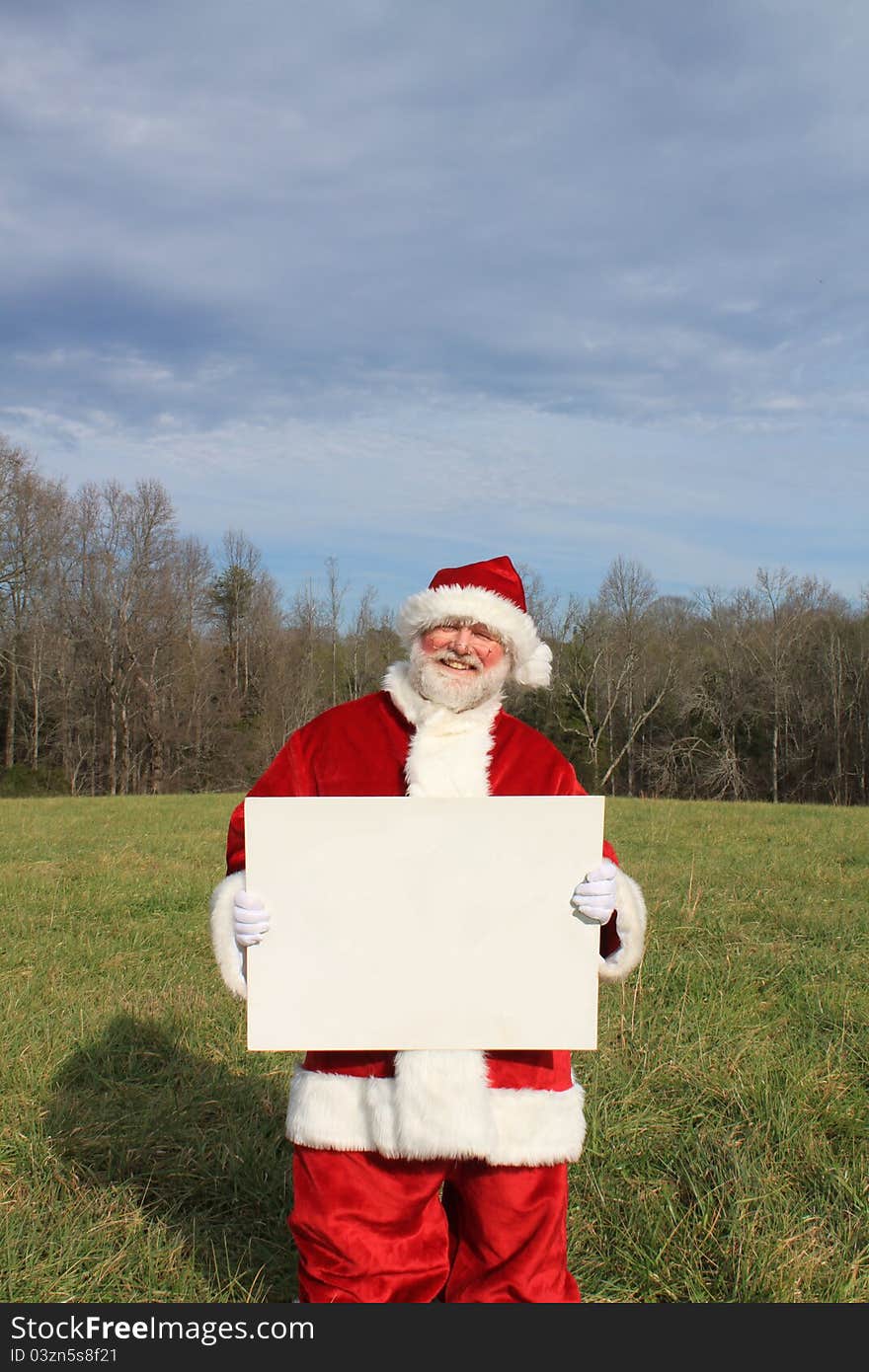 Santa Claus standing in a field holding a big white blank sign. Santa Claus standing in a field holding a big white blank sign.