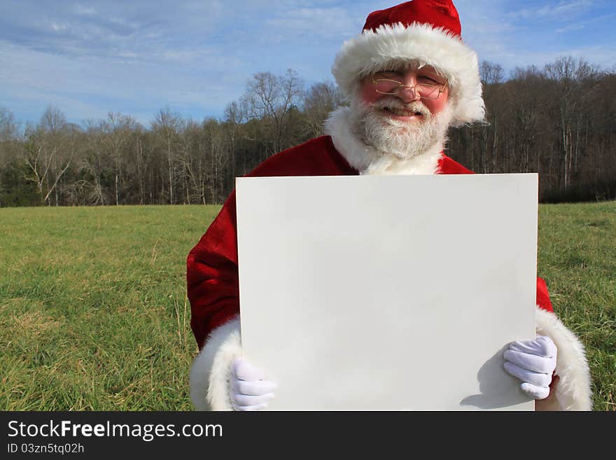 Santa Claus in an open field holding a large white sign.  Write your own message. Santa Claus in an open field holding a large white sign.  Write your own message.