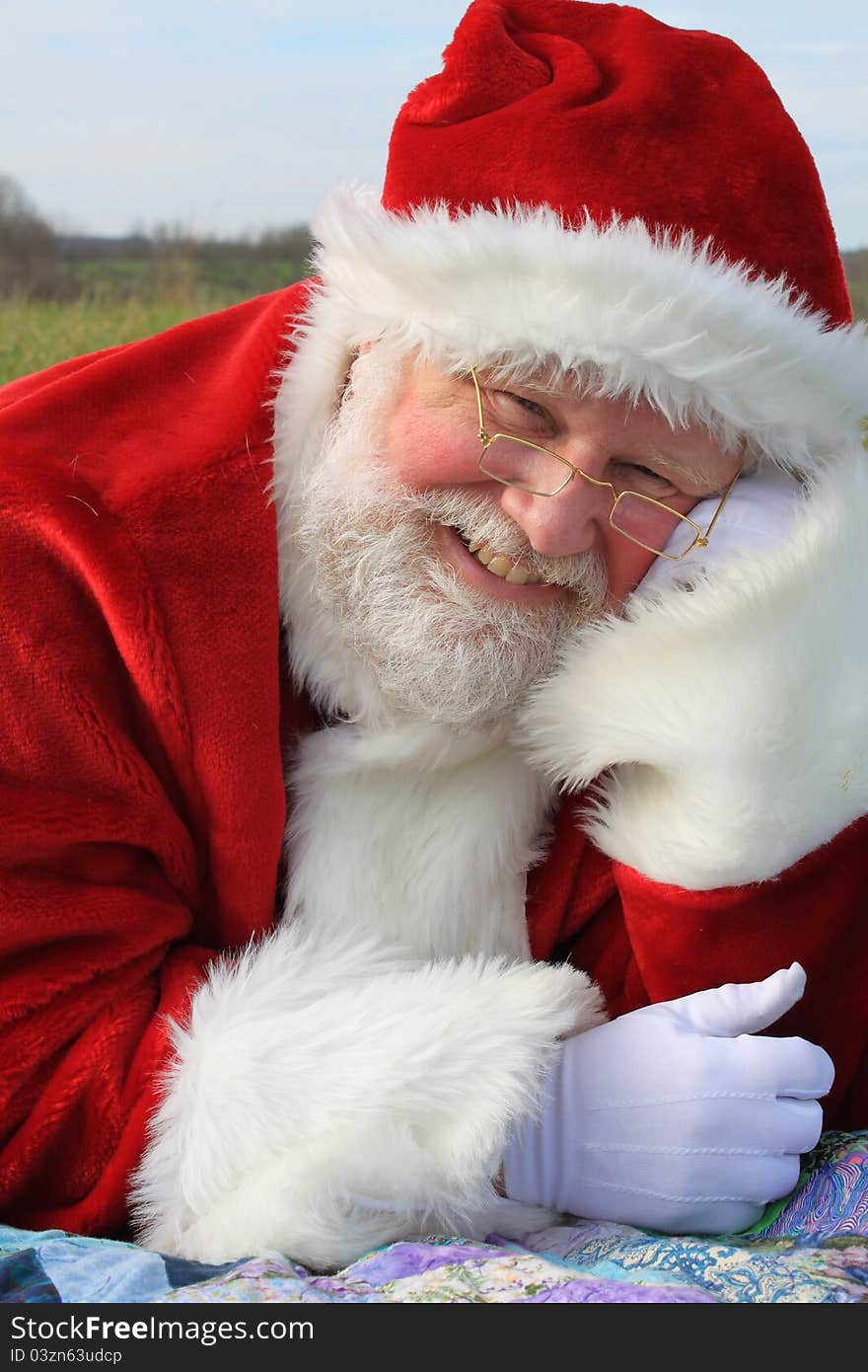 Santa Claus laying on a quilted blanket in an open field. In the background is a silo. Santa Claus laying on a quilted blanket in an open field. In the background is a silo.