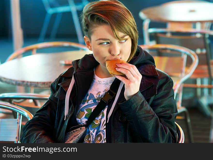 Portrait of stylish blond girl with eats burger on the terrace of the fast food. Portrait of stylish blond girl with eats burger on the terrace of the fast food