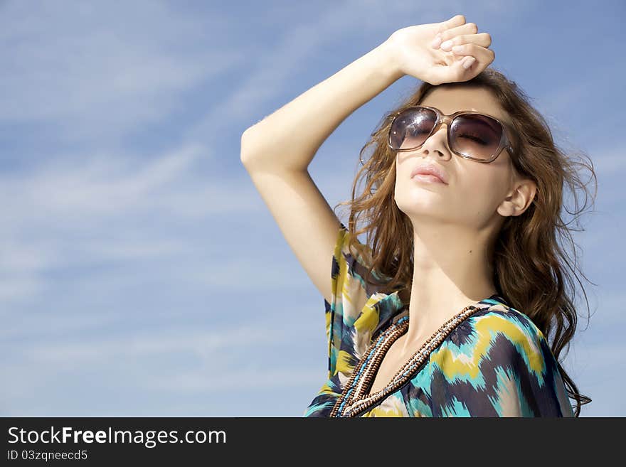 Portrait of beautiful brunette girl in sunglasses on background blue sky. Portrait of beautiful brunette girl in sunglasses on background blue sky