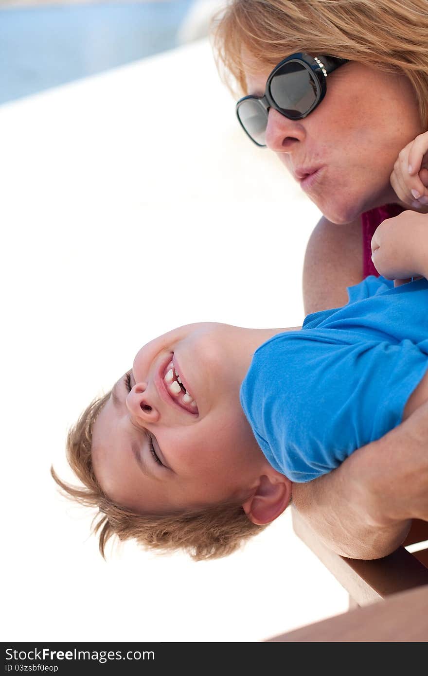 An older mother or young grandmother holds an 8 year old boy on her lap and pretends to kiss him. Boy is laughing hysterically with a huge smile. Image taken outdoors. An older mother or young grandmother holds an 8 year old boy on her lap and pretends to kiss him. Boy is laughing hysterically with a huge smile. Image taken outdoors.