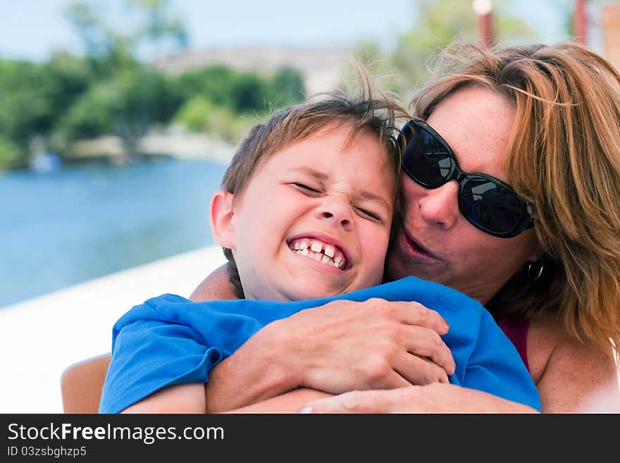 An older mother or young grandmother holds an 8 year old boy on her lap and pretends to kiss him. Boy is laughing hysterically with a huge smile. Image taken outdoors. An older mother or young grandmother holds an 8 year old boy on her lap and pretends to kiss him. Boy is laughing hysterically with a huge smile. Image taken outdoors.