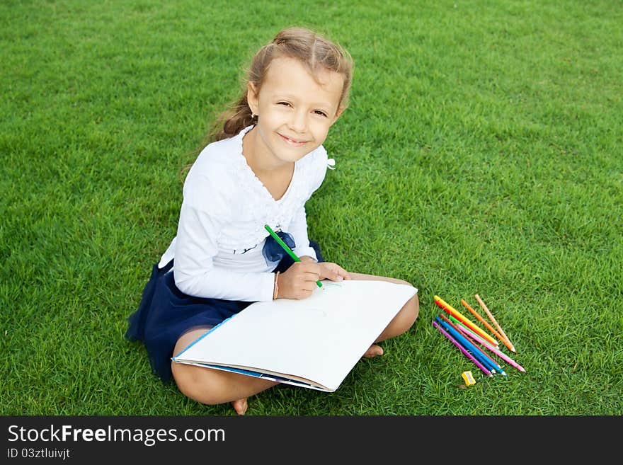 Little cute girl drawing with crayons sitting on a green lawn