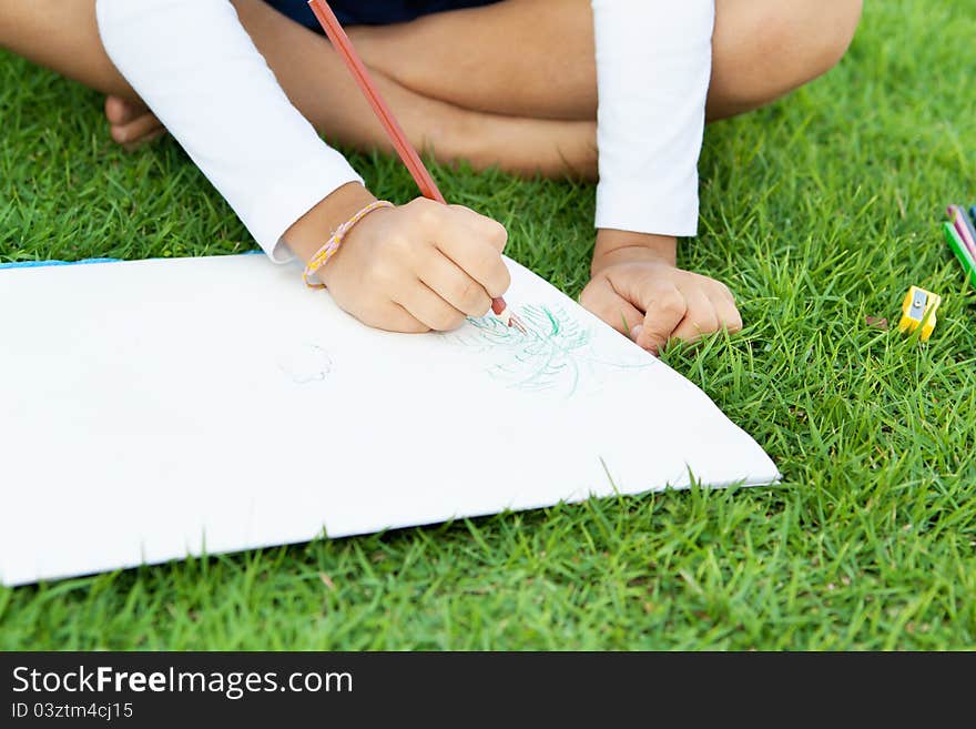 Little cute girl drawing with crayons sitting on a green lawn