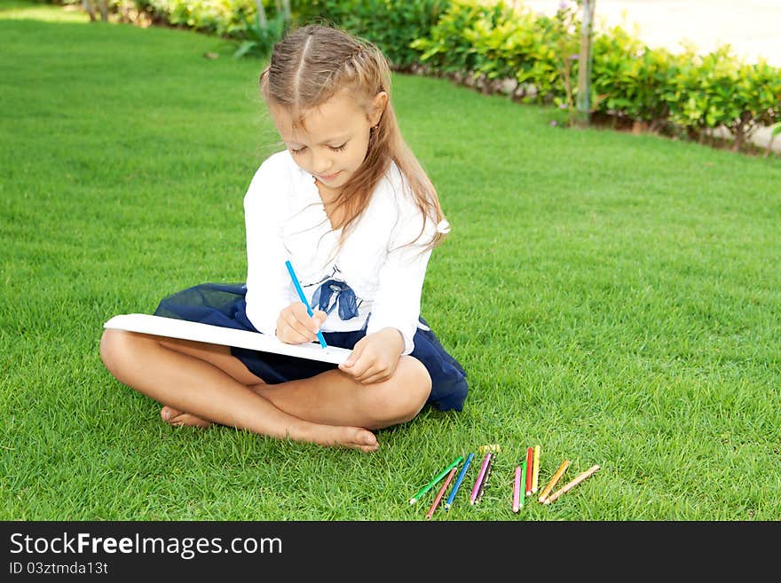 Little cute girl drawing with crayons sitting on a green lawn