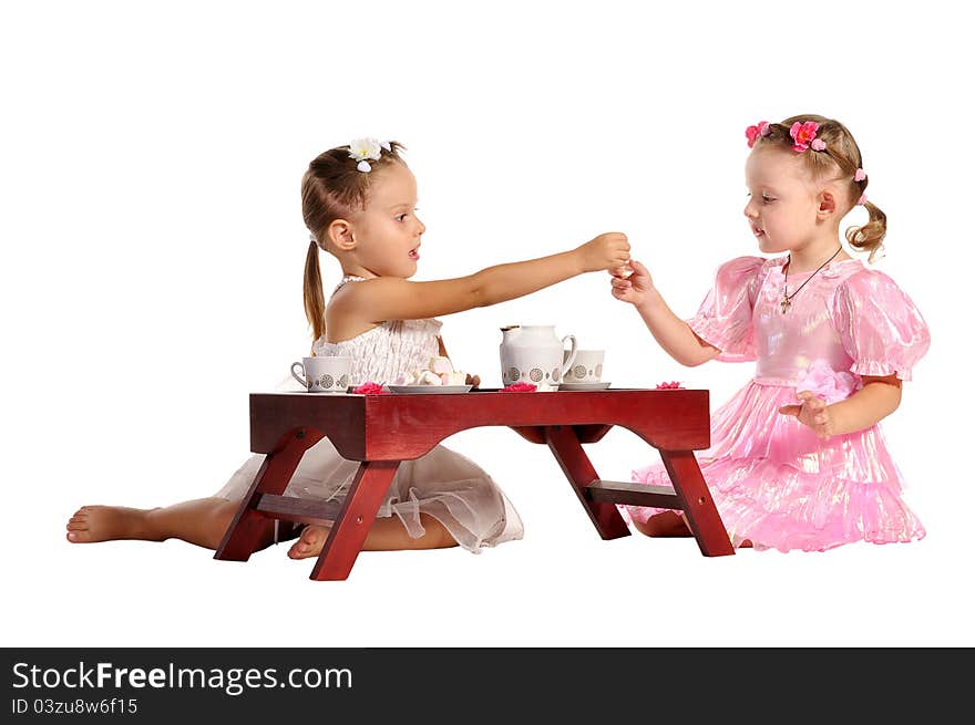 Two pretty twins sisters in beautiful dresses having tea wtih zephyr sitting at coffee table isolated on white background. Two pretty twins sisters in beautiful dresses having tea wtih zephyr sitting at coffee table isolated on white background