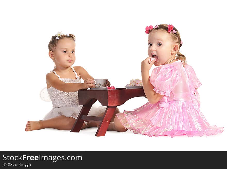 Two pretty twins sisters in beautiful dresses having tea wtih zephyr sitting at coffee table  isolated on white background. Two pretty twins sisters in beautiful dresses having tea wtih zephyr sitting at coffee table  isolated on white background