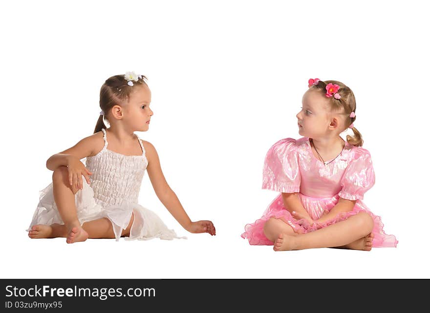 Two pretty twins sisters in beautiful dresses sitting barefooted and talking isolated on white background. Two pretty twins sisters in beautiful dresses sitting barefooted and talking isolated on white background