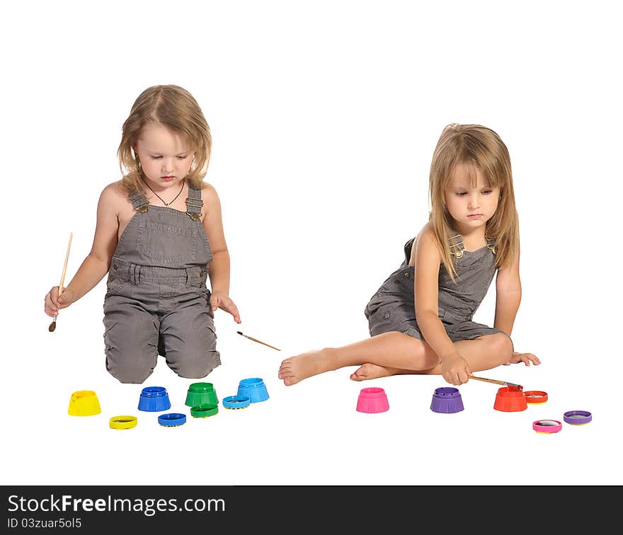 Two pretty barefooted twins sisters in rompers painting pictures with brushes isolated on white background. Two pretty barefooted twins sisters in rompers painting pictures with brushes isolated on white background