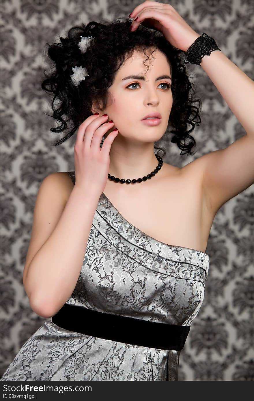 Brunette model with silver dress and white flowers in hair, hand on shoulder and hair, looking off camera. Brunette model with silver dress and white flowers in hair, hand on shoulder and hair, looking off camera