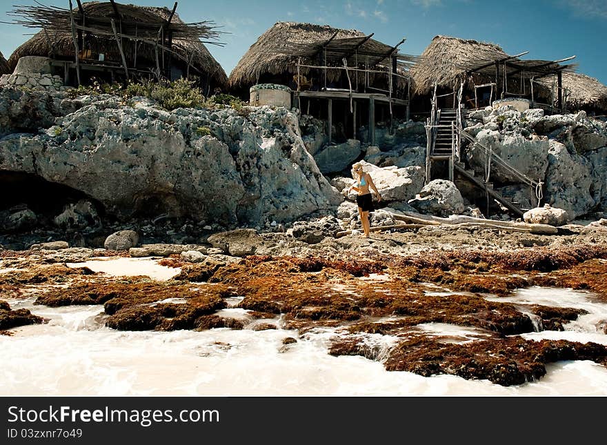 Woman walking on rocks in front of palapas built on cliffs in the Riviera Maya area of the Yucatan Peninsula. Woman walking on rocks in front of palapas built on cliffs in the Riviera Maya area of the Yucatan Peninsula.