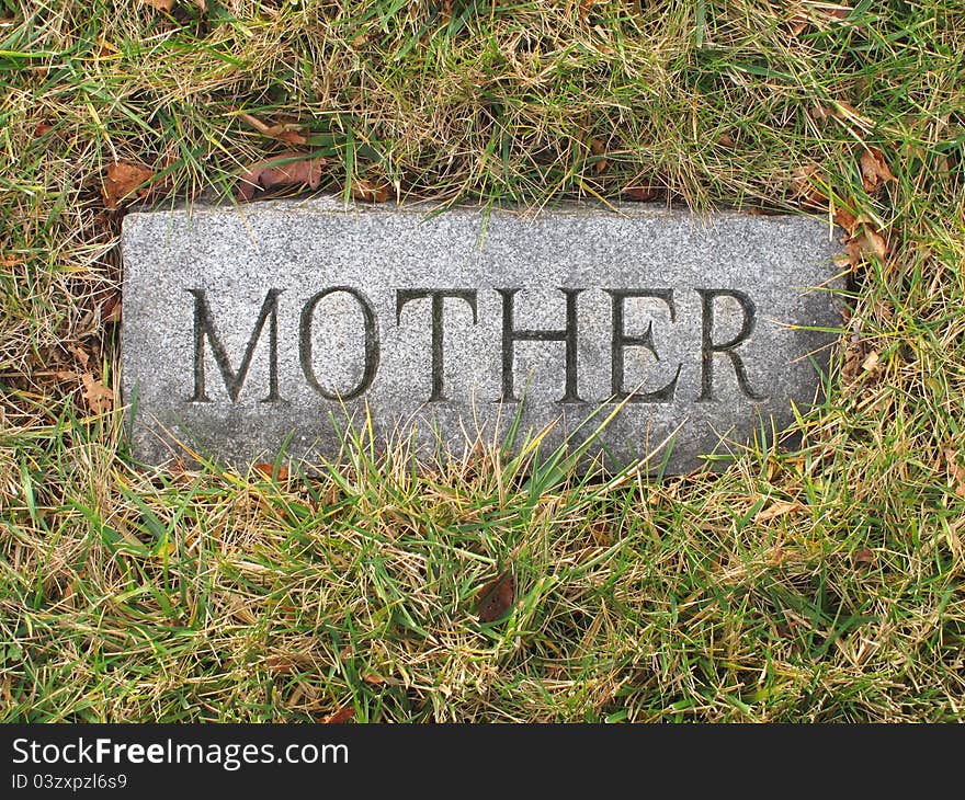 Vintage stone grave marker for a mother, buried in the ground surrounded by grass. Vintage stone grave marker for a mother, buried in the ground surrounded by grass.