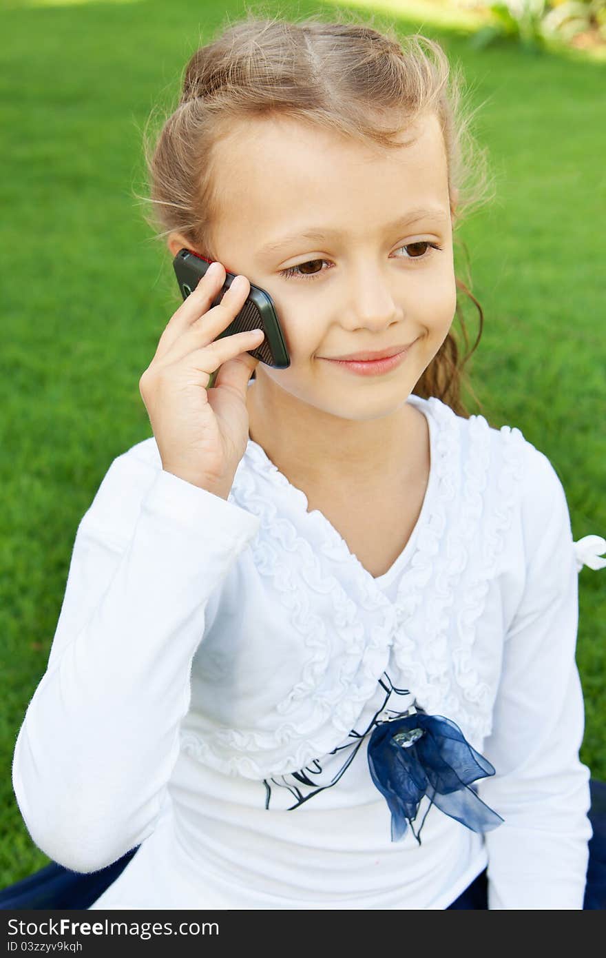 Little cute girl talking on a mobile phone while sitting on green grass. Little cute girl talking on a mobile phone while sitting on green grass