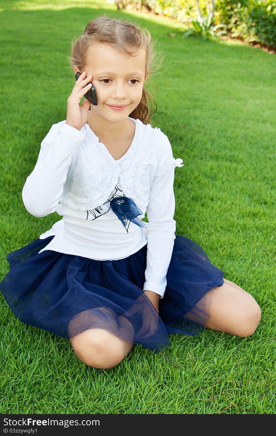 Little cute girl talking on a mobile phone while sitting on green grass. Little cute girl talking on a mobile phone while sitting on green grass